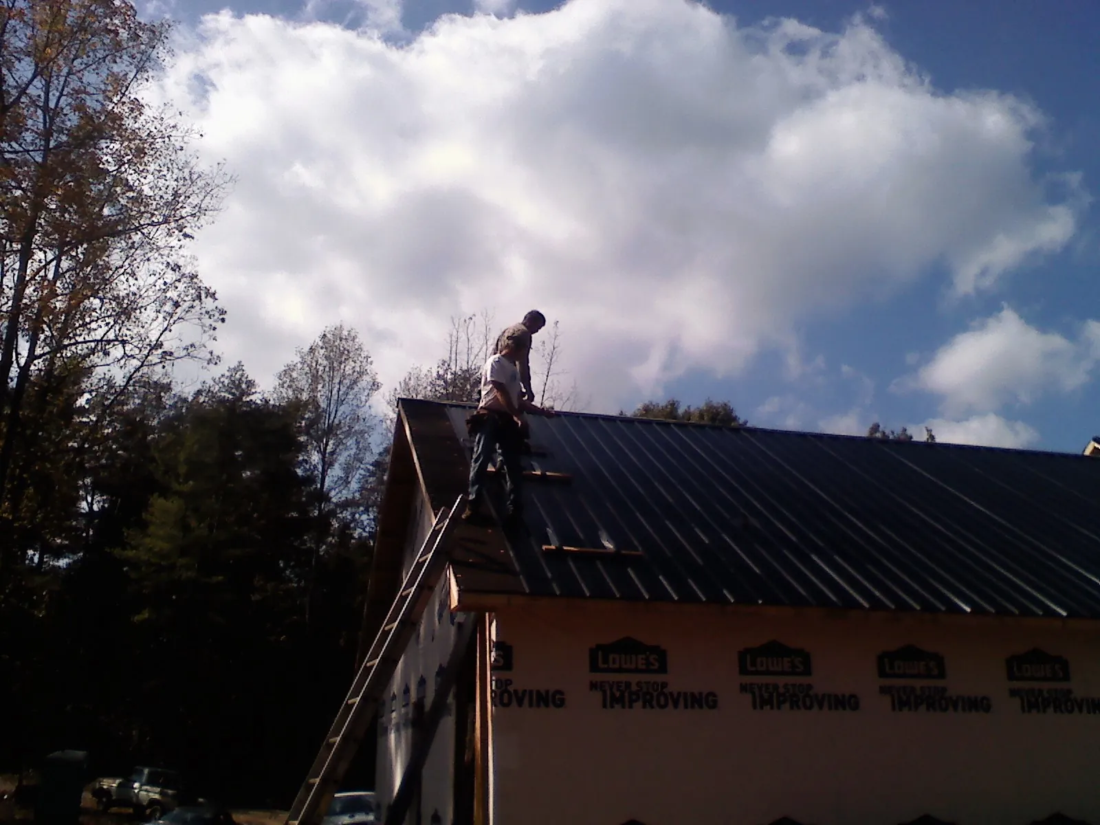 Roofer fastening dark metal panels high against a cloudy sky, from a Roof Inspection job in Rosendale